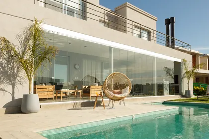 Fachada moderna con piscina y silla colgante de rattan — proyecto TOLDER - CERRAMIENTOS, por Argentina en Obra 2024, en Rincón de Milberg