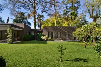Fachada moderna con amplios ventanales y jardín frondoso — proyecto Casa M, por Estudio Dado, en Pilar