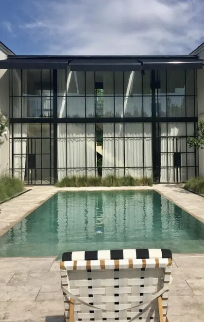 Piscina moderna con fachada de vidrio y sillón a rayas — proyecto CASA DEL PUENTE, por Estudio Xime Fontan Balestra, en General Pacheco