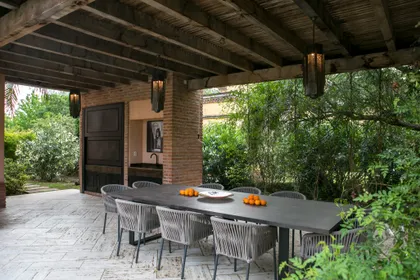 Quincho con mesa y sillas bajo pérgola de madera, rodeado de vegetación — proyecto CasaLA, por Ricardo Pereyra Iraola 