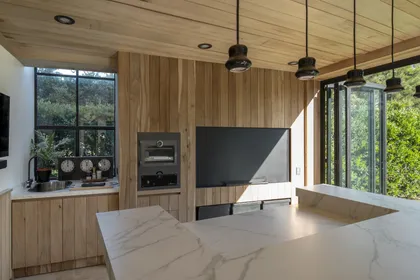 Cocina moderna de madera con isla de mármol y ventanales al bosque — proyecto Quincho PG, por Estudio Lak