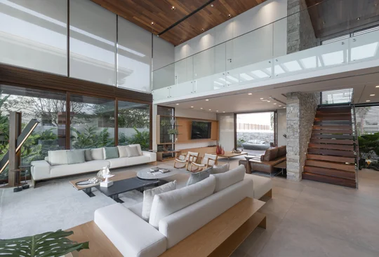 living con doble altura, sofás blancos y grandes ventanales — proyecto Casa C.A.P., por Ruschel Arquitetura e Urbanism