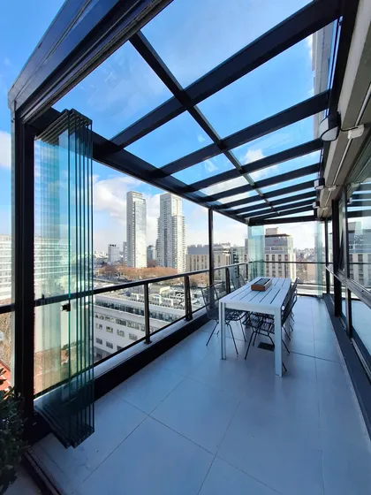 Terraza moderna con vistas urbanas y paredes plegables de cristal — proyecto TOLDER - CERRAMIENTOS, por Argentina en Obra 2024, en Rincón de Milberg