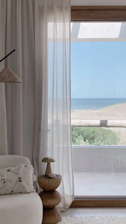 Living con vista al mar, cortinas de lino y sillón texturizado — proyecto El Refugio, por Grupo Pauta Arquitectura, en Pinamar
