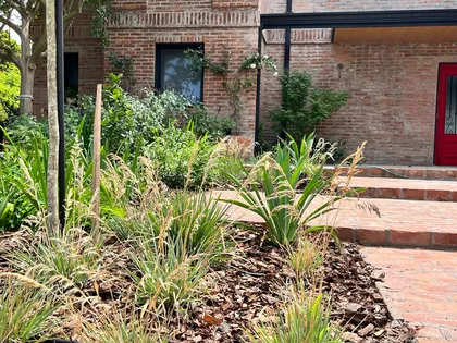 Fachada moderna rústica con ladrillos a la vista y mucha vegetación — proyecto Proyecto CARDALES, por Celina Sammartino Paisajismo, en Los Cardales