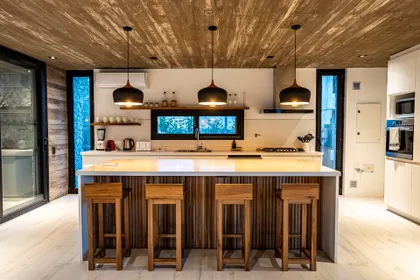 Cocina moderna con isla, techo de madera y luces colgantes — proyecto casa la huella, por Guerrero Arquitectos, en Pinamar