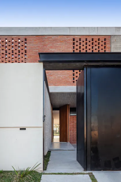 Fachada moderna con ladrillo perforado y puerta pivotante de madera — proyecto CASA BSB, por BUSCETTI & DI BERNARDO arquitectas, en Gonnet