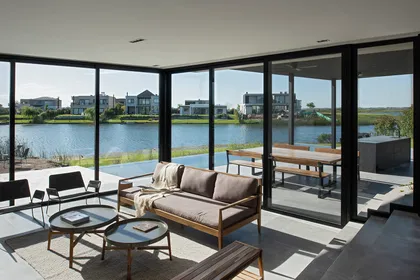 Living moderno con vistas al agua y ventanales gigantes — proyecto CASA MUELLES, por GMARQ, en Escobar