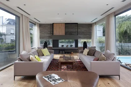 Living moderno con grandes ventanales y mobiliario beige — proyecto Acasusso, por Remy Arquitectos, en Acassuso