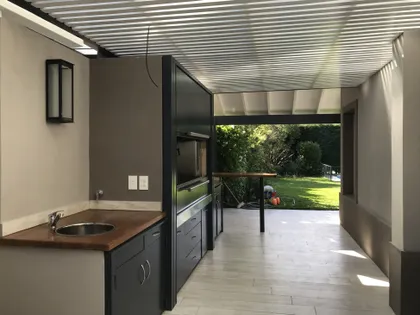 Quincho moderno con parrilla empotrada y techo metálico — proyecto Casa Beccar, por Rioja Arquitectura, en Béccar