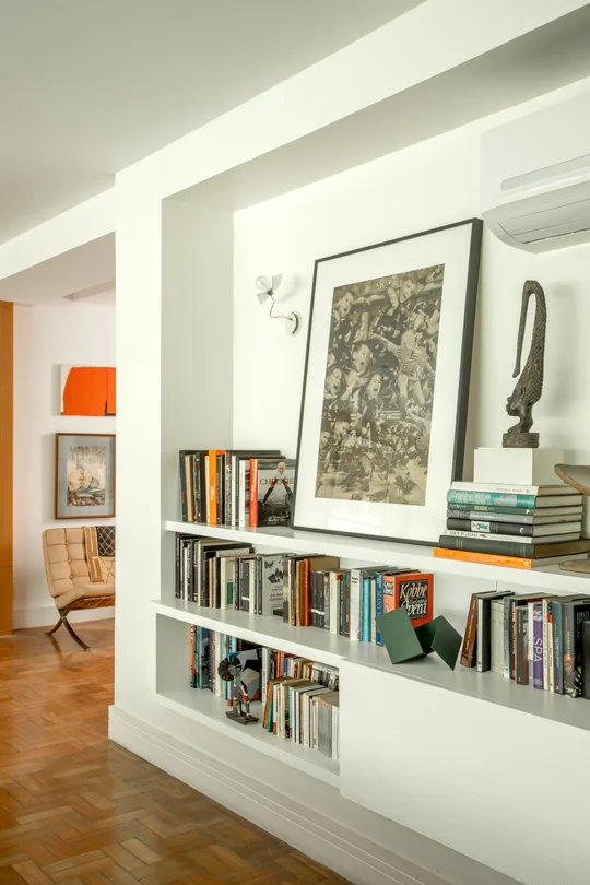 Pasillo blanco con estantería integrada, libros y arte contemporáneo — proyecto Apartamento PM, por Patrícia Marinho Arquitetura 