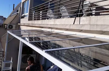 Fachada moderna con pérgola de vidrio y concreto expuesto — proyecto Techos Blindex, por Cristalcenter, en Buenos Aires