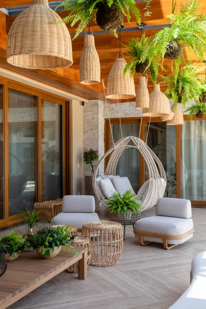 Terraza semiexterior con deck de madera, luces colgantes y sillas de ratán — proyecto Projeto Destaque Club&Casa, por OKA ARQUITETURA
