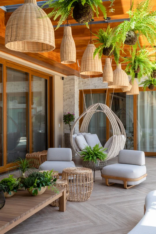 Terraza semiexterior con deck de madera, luces colgantes y sillas de ratán — proyecto Projeto Destaque Club&Casa, por OKA ARQUITETURA