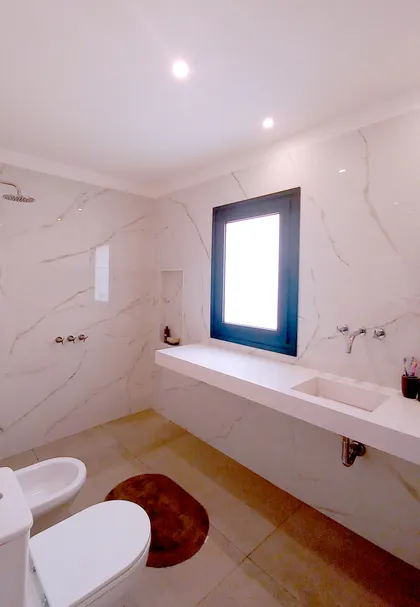 Baño moderno con paredes de mármol, mesada flotante y sanitarios blancos — proyecto Casa CG191, por EZ architects, en Belén de Escobar