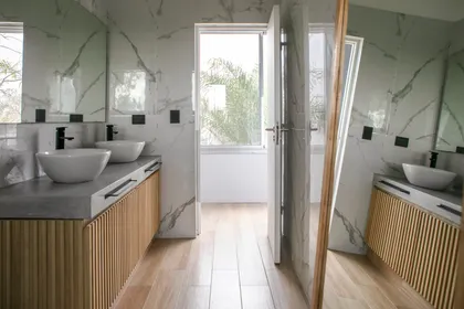 Baño moderno con mármol, madera acanalada y grifería negra — proyecto Obra El Encuentro, por Arq. Lourdes Yarade Saravia, en Benavidez
