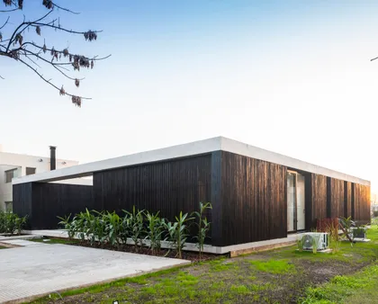 fachada moderna de madera oscura y techo blanco con vegetación — proyecto Casa ROMA, por V2 Arquitectos, en City Bell
