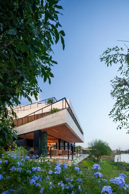 fachada moderna con piedra beige y vegetación exuberante — proyecto Casa Porsche, por Remy Arquitectos, en Buenos Aires
