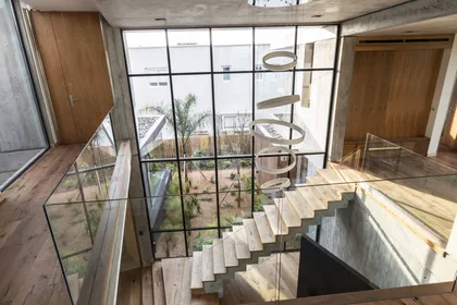 Atrio moderno a doble altura con escalera flotante y jardín interior — proyecto Casa CZ, por Estudio Juan Trivelloni