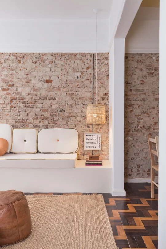 Living moderno con pared de ladrillo, sofá blanco y piso de madera — proyecto Roomie Coliving, por Camila Cavalheiro Arquiteta