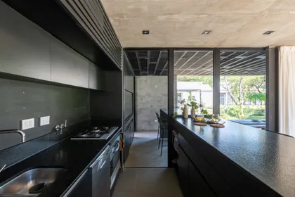 Cocina moderna negra con isla, ventanales hacia jardin exterior — proyecto Casa SI, por Grupo Studio, en Villa Allende