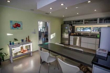 Cocina moderna con comedor integrado, paredes verdes, muebles blancos y mesa oscura — proyecto Vivienda Unifamiliar en Pinamar, por Estudio Schifano, en Pinamar