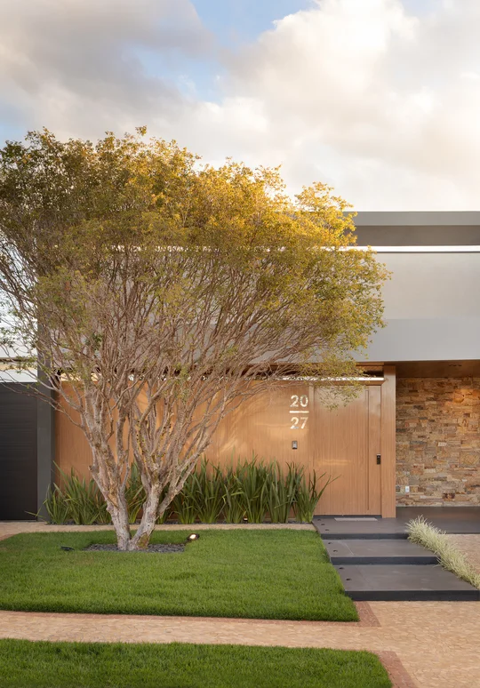 Casa contemporánea con árbol dorado, fachada ladrillo y acceso principal — proyecto Casa Lago Sul, por Daniel Santo