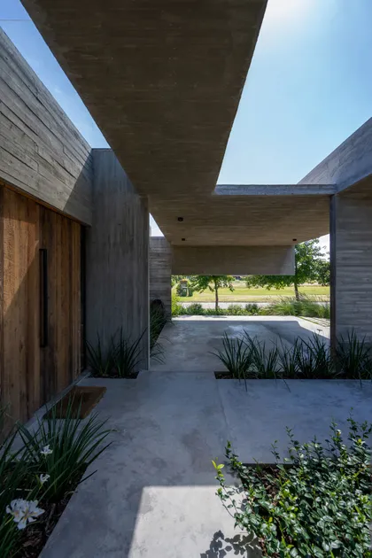 Fachada moderna de hormigón con amplias losas y vegetación integrada — proyecto Casa Tres Patios, por Besonías Almeida arquitectos, en Pilar