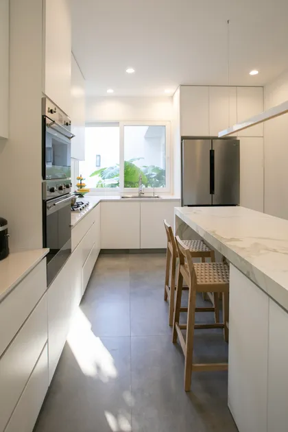 Cocina moderna blanca con isla de mármol y suelo de microcemento — proyecto Obra Newman FH, por Arq. Lourdes Yarade Saravia, en Benavidez