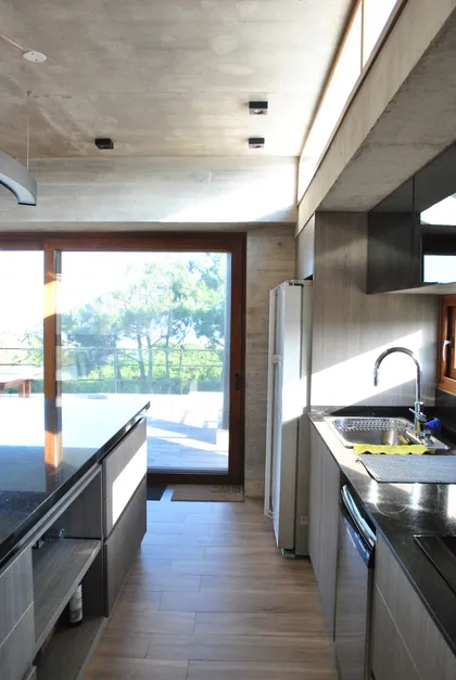 Cocina moderna con techo de hormigón y ventanales amplios — proyecto Casa FSC, por TAVA Coop, en Pinamar