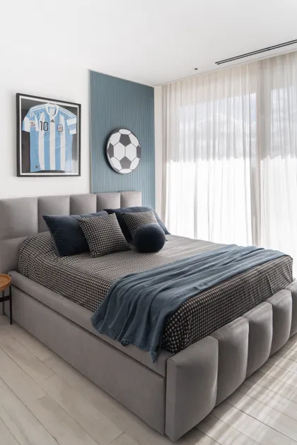 Dormitorio moderno con cama tapizada, camiseta de fútbol y cortinas blancas — proyecto PROYECTO NAUDIR II, por July Acosta Home, en Belén de Escobar