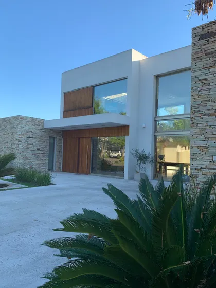 Fachada moderna con piedra, vidrio y madera — proyecto CASA LR 56 - SOFITEL LOS CARDALES  , por Carolina Depetris, en Los Cardales