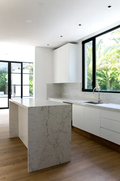 Cocina moderna con isla mármol blanca, grandes ventanales y pisos de madera — proyecto Bosque Chico, por Estudio Arq. María Sioli, en Garin