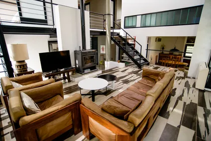 Living moderno de doble altura con escalera flotante y sofá de cuero — proyecto CASA GONNET, por LEONE LORAY ARQUITECTOS, en Gonnet