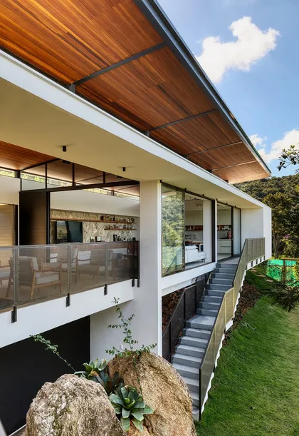 Fachada contemporánea con terraza, techo madera y grandes ventanales — proyecto Casa das Pedras, por Tetro Arquitetura