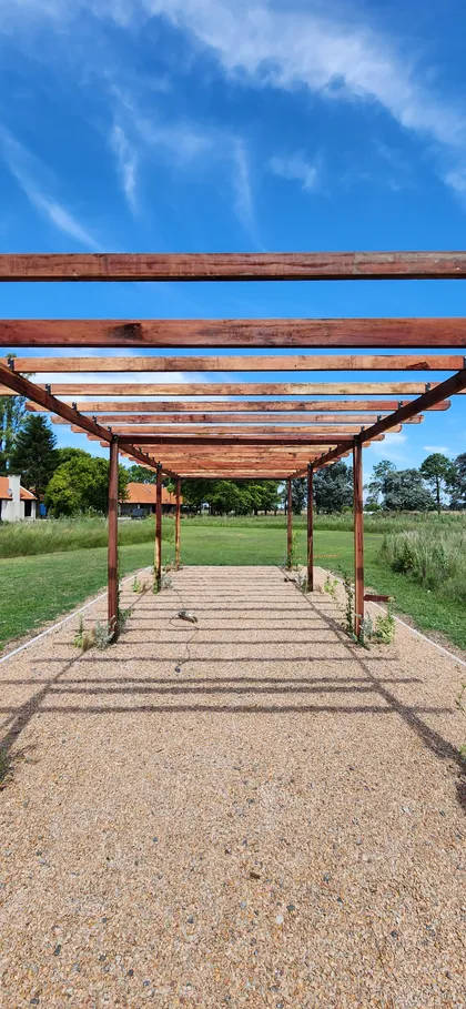 pérgola de madera rústica en patio de grava — proyecto Casa COAL, por Estudio Rifahi, en B2814 Los Cardales