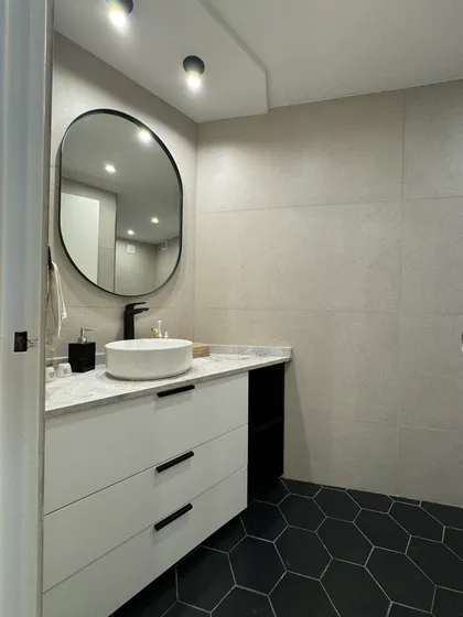 Baño moderno con espejo ovalado, vanitory blanco y pisos hexagonales negros — proyecto Las Heras, por MDBK Arquitectura, en Palermo