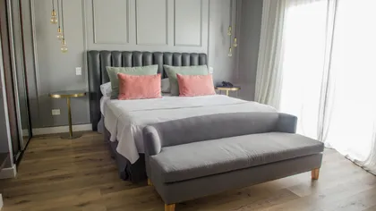 Dormitorio moderno con cama grande, banco y detalles dorados — proyecto Villa Isidro Hotel Boutique & Spa, por Hermann Arquitectos, en San Isidro