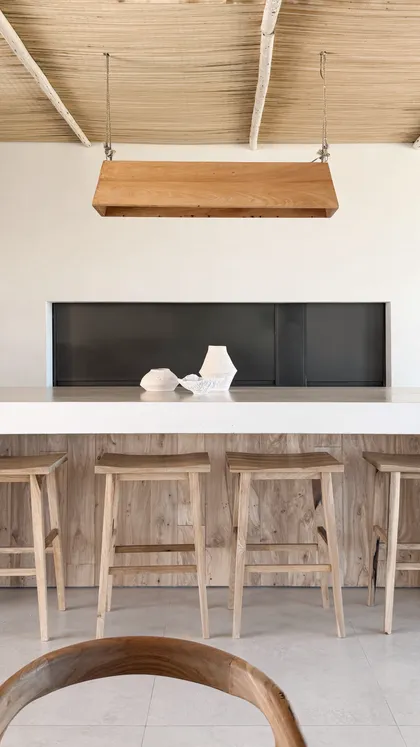 Cocina minimalista con isla de mármol, bancos de madera y lámpara colgante de madera — proyecto El Refugio, por Grupo Pauta Arquitectura, en Pinamar