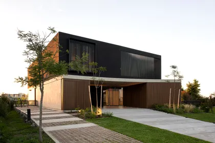 Casa moderna con fachada de madera y metal negro y ventanas amplias — proyecto CASA MUELLES, por GMARQ, en Escobar