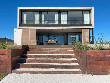 Fachada moderna con revestimiento de madera y grandes ventanales — proyecto El Secreto, por Grupo Pauta Arquitectura, en Tigre