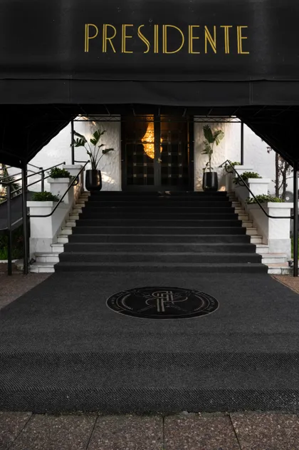 Entrada de fachada comercial con escaleras de alfombra negra y letrero dorado — proyecto PRESIDENTE BAR HIPODROMO, por AB ARQUITECTURA, en San Isidro