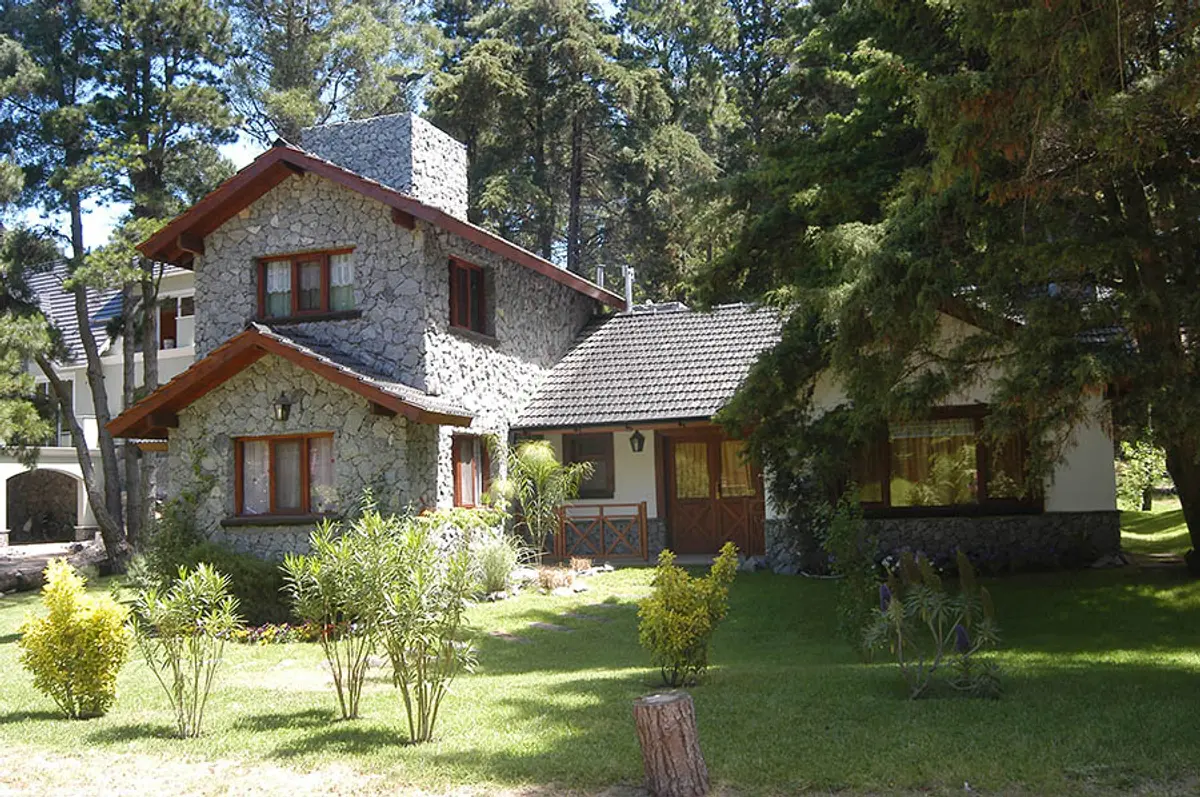Fachada rústica de pedra e madeira na floresta — projeto Casa Cariló 2003 - 2, por Hugo Zawadski Arquitectos, em Cariló