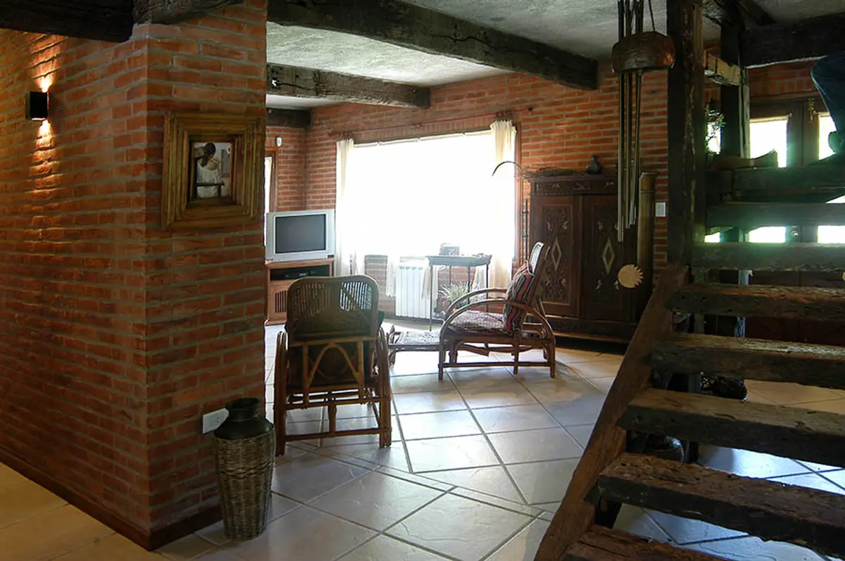 Sala rústica con ladrillos expuestos y vigas de madera — proyecto Casa Cariló 2004, por Hugo Zawadski Arquitectos, en Cariló