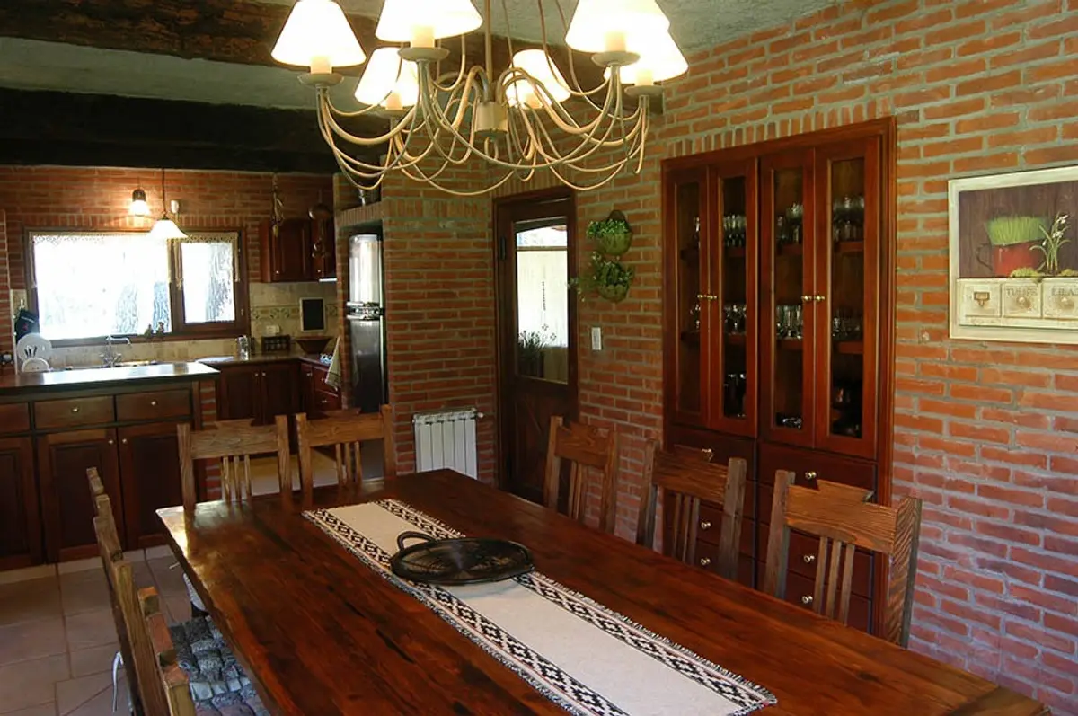 Sala de jantar rústica com tijolos aparentes e cozinha adjacente — projeto Casa Cariló 2004, por Hugo Zawadski Arquitectos, em Cariló