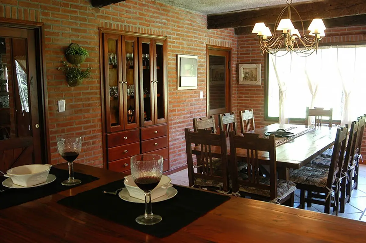Sala de jantar rústica com paredes de tijolo aparente e vigas de madeira — projeto Casa Cariló 2004, por Hugo Zawadski Arquitectos, em Cariló