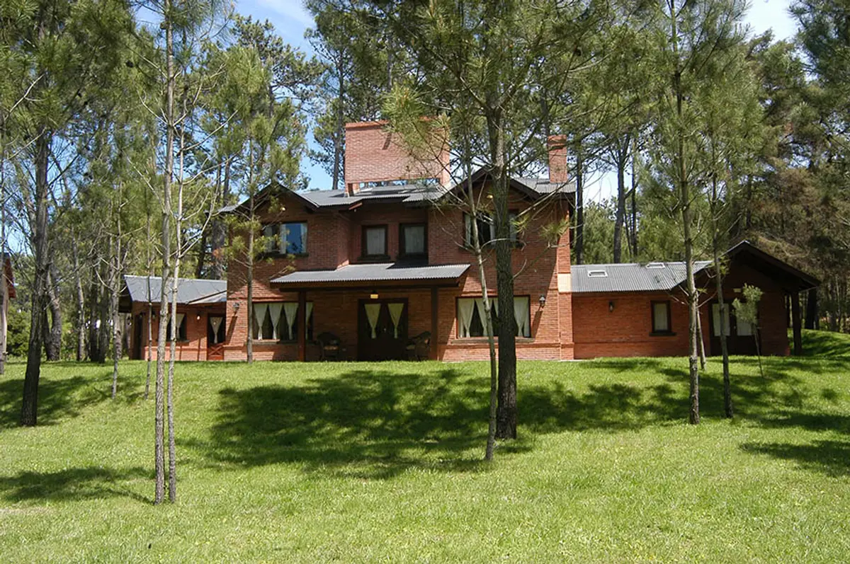 Fachada de casa de campo de tijolos vermelhos com árvores e gramado — projeto Casa Cariló 2004, por Hugo Zawadski Arquitectos, em Cariló