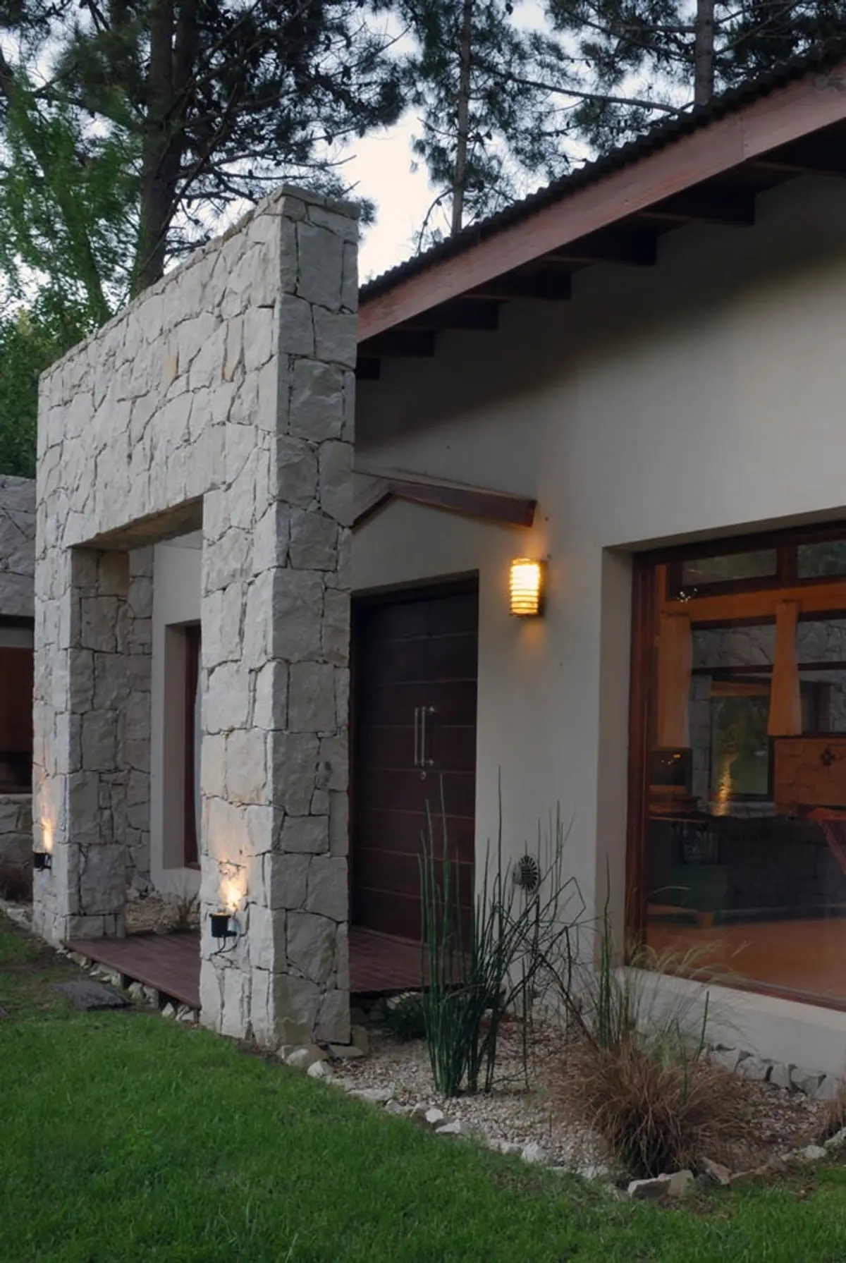 Fachada moderna com muro de pedra rústica e luzes externas — projeto Casa Cariló 2006, por Hugo Zawadski Arquitectos, em Cariló