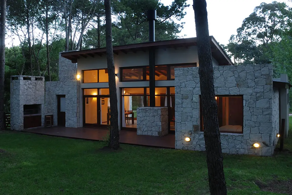 Fachada moderna de piedra y madera con amplios ventanales — proyecto Casa Cariló 2006, por Hugo Zawadski Arquitectos, en Cariló