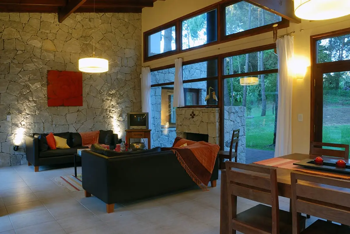 Sala de estar moderna rústica com paredes de pedra e janelas para floresta — projeto Casa Cariló 2006, por Hugo Zawadski Arquitectos, em Cariló